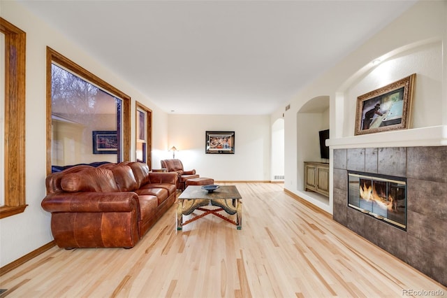 living area featuring visible vents, baseboards, light wood-style flooring, and a tile fireplace