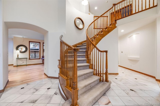 stairs featuring a high ceiling, baseboards, and arched walkways