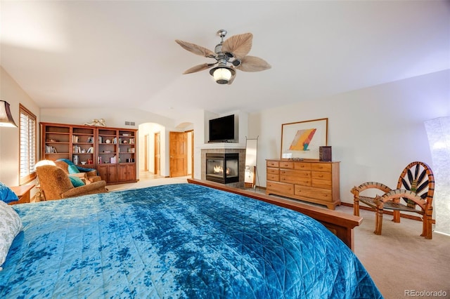 bedroom featuring a ceiling fan, carpet floors, lofted ceiling, arched walkways, and a tile fireplace