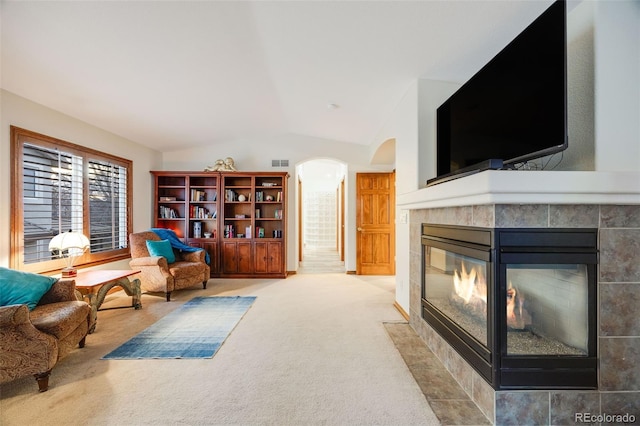 sitting room featuring visible vents, a tiled fireplace, arched walkways, carpet flooring, and lofted ceiling