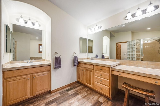 bathroom featuring a shower stall, wood finished floors, two vanities, and a sink