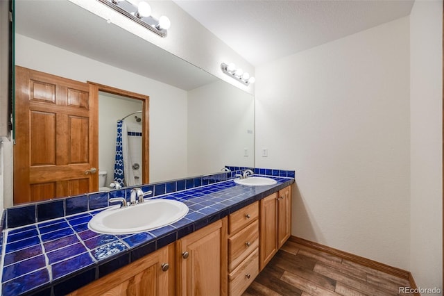 full bath with a sink, baseboards, wood finished floors, and double vanity