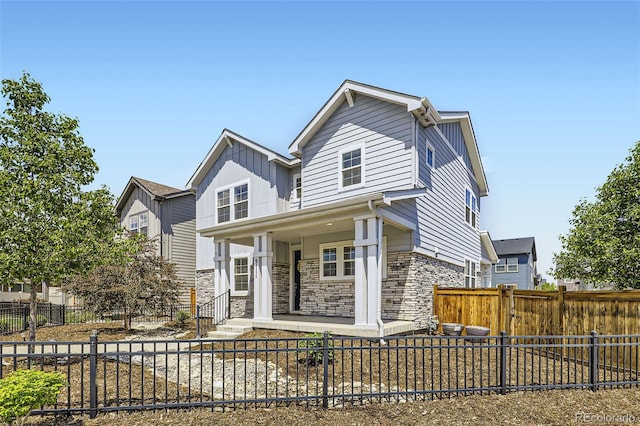 view of front of home with a porch, stone siding, a fenced front yard, and board and batten siding