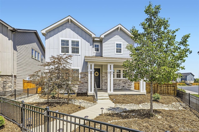 view of front facade featuring board and batten siding, stone siding, a porch, and a fenced backyard