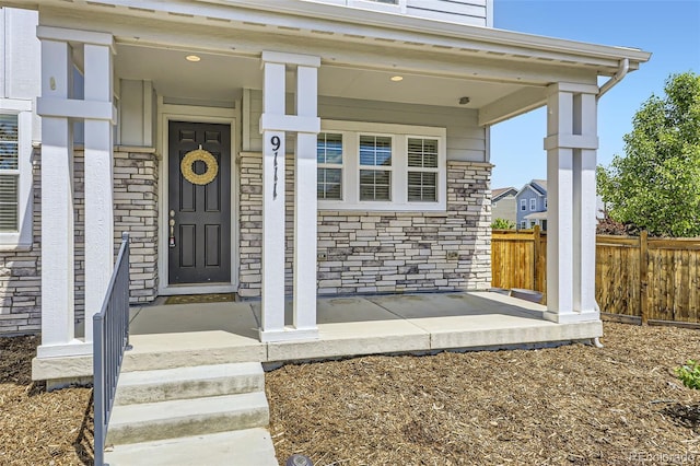 view of exterior entry featuring stone siding and fence