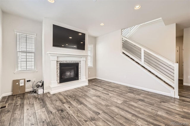 unfurnished living room featuring stairway, wood finished floors, recessed lighting, baseboards, and a glass covered fireplace