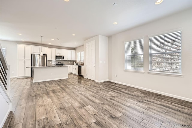 unfurnished living room featuring healthy amount of natural light, wood finished floors, recessed lighting, and baseboards