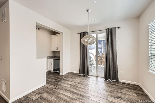 unfurnished dining area featuring beverage cooler, dark wood finished floors, and baseboards