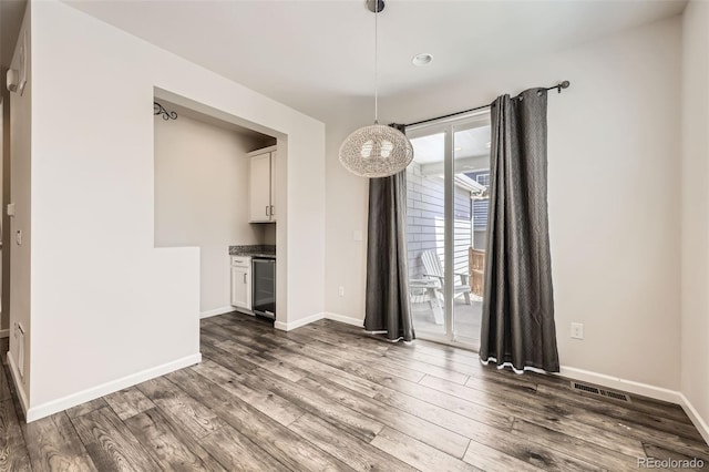 unfurnished dining area with dark wood-type flooring, wine cooler, and baseboards