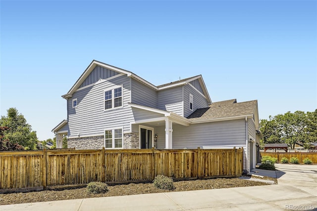 view of front of house featuring a fenced front yard, board and batten siding, stone siding, concrete driveway, and a shingled roof