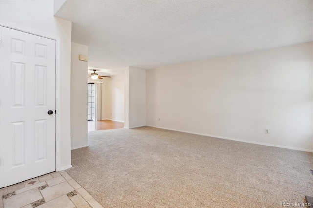 empty room with light colored carpet, baseboards, a ceiling fan, and a textured ceiling