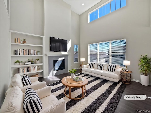 living area featuring baseboards, a towering ceiling, a glass covered fireplace, and wood finished floors