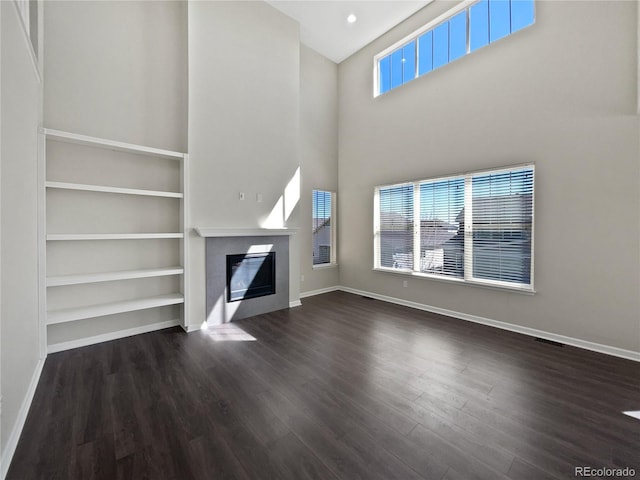 unfurnished living room with dark wood-style floors, a healthy amount of sunlight, baseboards, and a glass covered fireplace