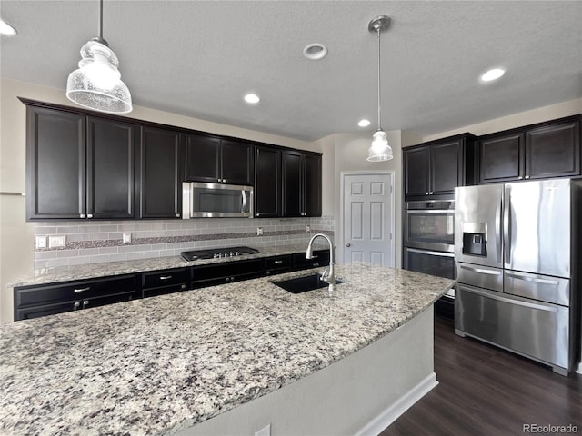 kitchen with stainless steel appliances, a sink, dark wood finished floors, decorative backsplash, and light stone counters