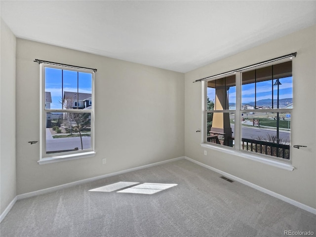 empty room featuring plenty of natural light, carpet floors, visible vents, and baseboards