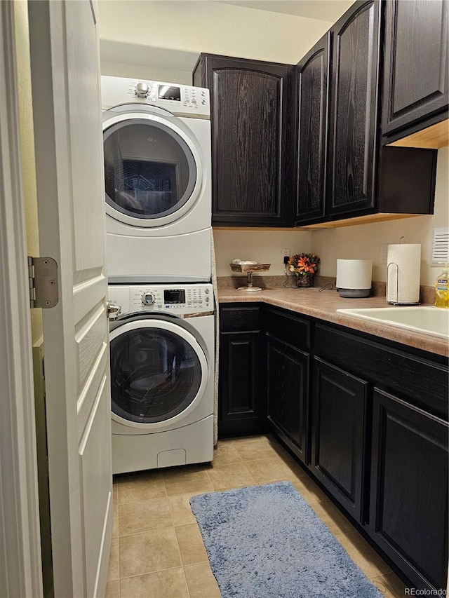 clothes washing area with sink, light tile patterned floors, cabinets, and stacked washer / drying machine