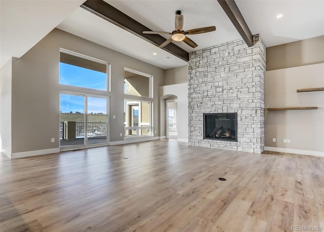 unfurnished living room with beamed ceiling, ceiling fan, a fireplace, and light hardwood / wood-style floors