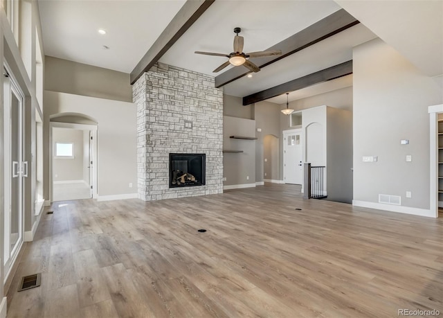 unfurnished living room with ceiling fan, a stone fireplace, beamed ceiling, and light wood-type flooring