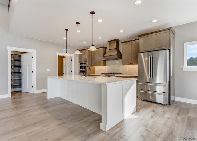 kitchen featuring premium range hood, appliances with stainless steel finishes, pendant lighting, sink, and a center island with sink