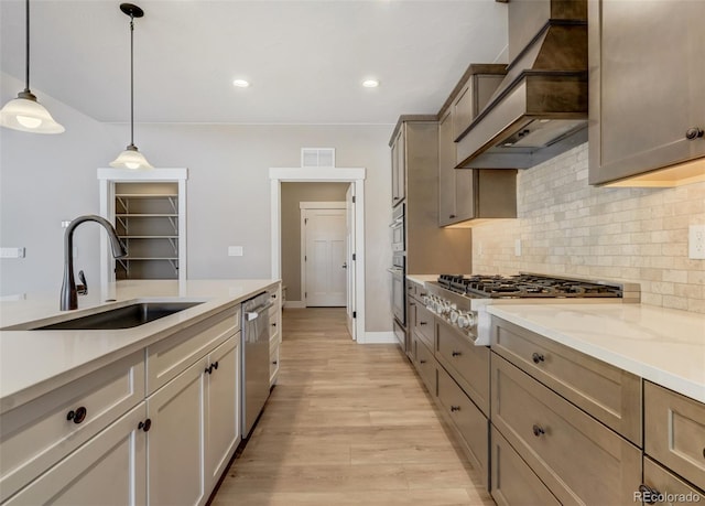 kitchen with sink, custom exhaust hood, decorative light fixtures, appliances with stainless steel finishes, and light hardwood / wood-style floors