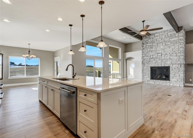 kitchen with sink, decorative light fixtures, stainless steel dishwasher, beam ceiling, and a kitchen island with sink