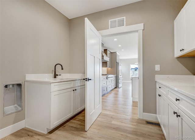 kitchen featuring light stone counters, wall chimney exhaust hood, white cabinets, and light wood-type flooring