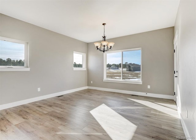 empty room with a wealth of natural light, an inviting chandelier, and light hardwood / wood-style floors