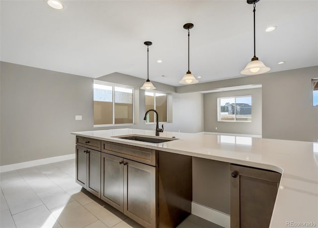 kitchen featuring light tile patterned flooring, dark brown cabinetry, decorative light fixtures, and sink