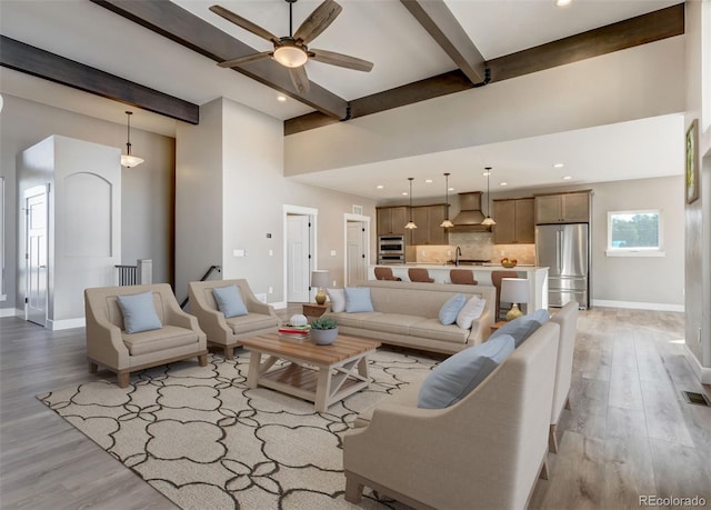 living room featuring beamed ceiling, ceiling fan, sink, and light hardwood / wood-style floors