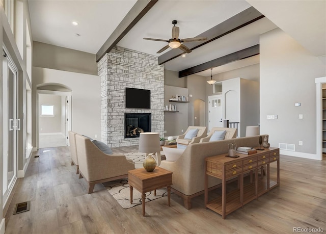 living room featuring beamed ceiling, ceiling fan, a fireplace, and light wood-type flooring