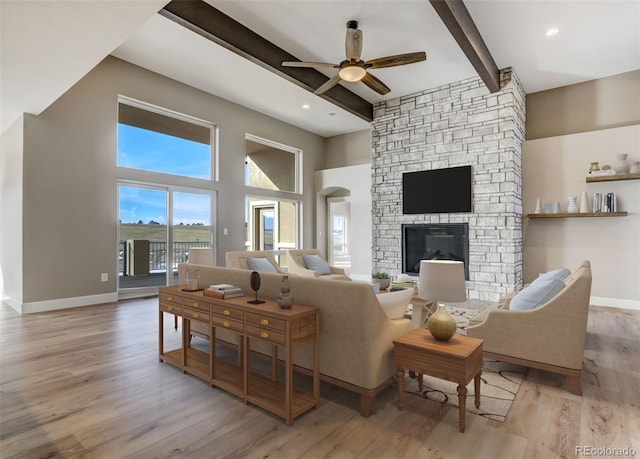 living room with ceiling fan, beam ceiling, a stone fireplace, and light hardwood / wood-style flooring