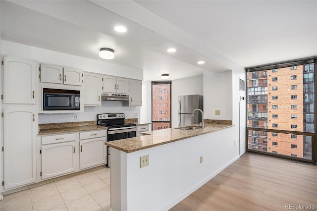 kitchen featuring a peninsula, light stone countertops, under cabinet range hood, a sink, and stainless steel appliances