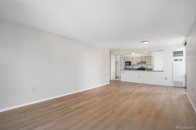 unfurnished living room featuring a heating unit, baseboards, visible vents, and light wood finished floors