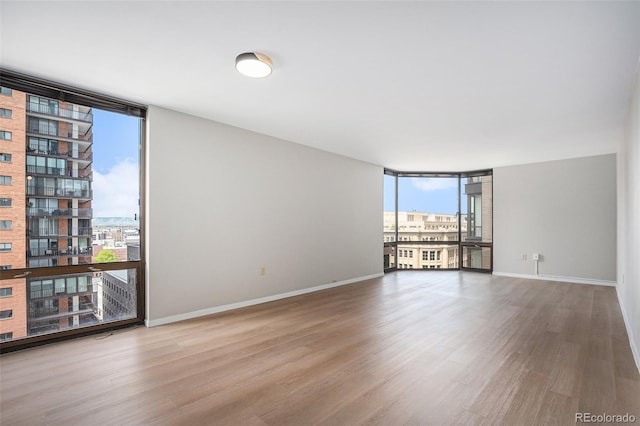 unfurnished room with a view of city, baseboards, expansive windows, and wood finished floors