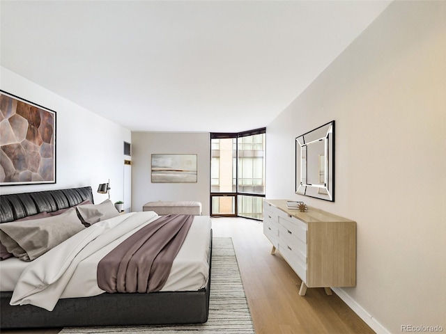 bedroom with expansive windows, light wood finished floors, and baseboards