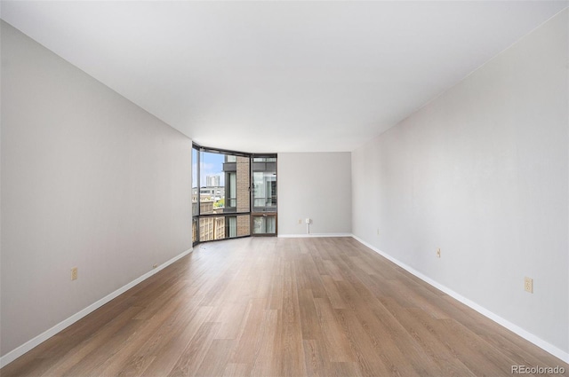 empty room featuring baseboards, floor to ceiling windows, and light wood-style floors