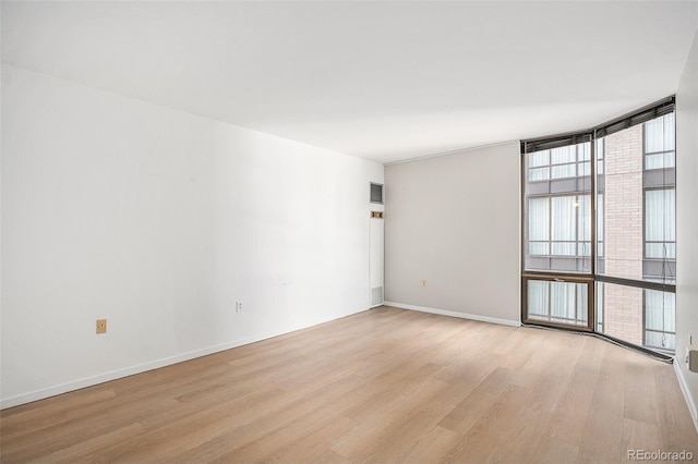 empty room featuring baseboards, floor to ceiling windows, and light wood-style floors