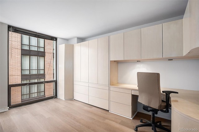 unfurnished office featuring floor to ceiling windows, built in study area, and light wood-type flooring