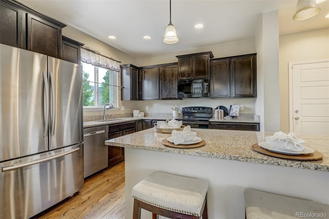 kitchen featuring light stone counters, sink, black appliances, light hardwood / wood-style flooring, and hanging light fixtures