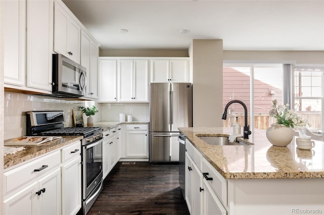 kitchen featuring appliances with stainless steel finishes, white cabinetry, sink, a kitchen island with sink, and light stone countertops