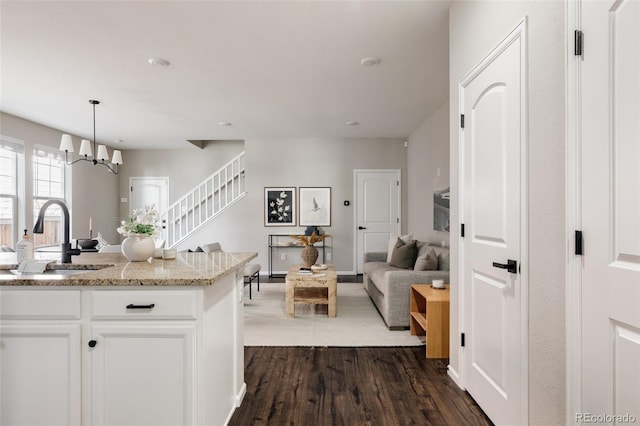 kitchen with dark hardwood / wood-style floors, pendant lighting, sink, white cabinets, and light stone countertops