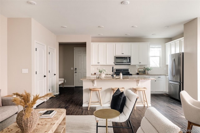 kitchen with white cabinetry, appliances with stainless steel finishes, light stone countertops, and an island with sink