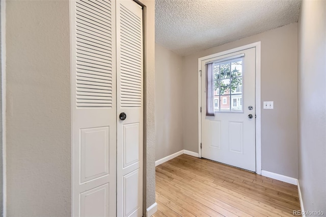 entryway with a textured wall, baseboards, light wood-style floors, and a textured ceiling