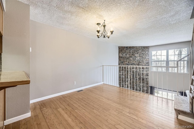 unfurnished room featuring visible vents, baseboards, a chandelier, hardwood / wood-style floors, and a textured ceiling