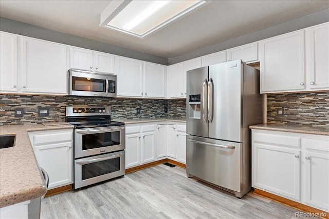 kitchen featuring appliances with stainless steel finishes, white cabinets, backsplash, and light wood-style flooring
