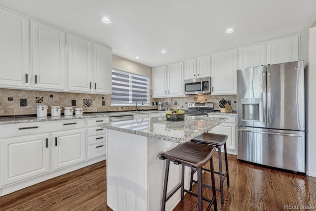 kitchen with dark hardwood / wood-style flooring, white cabinetry, light stone counters, a kitchen island, and stainless steel appliances