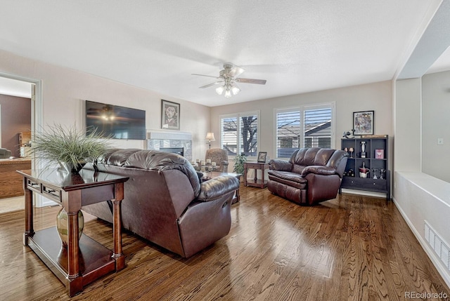 living room with a fireplace, hardwood / wood-style flooring, a textured ceiling, and ceiling fan