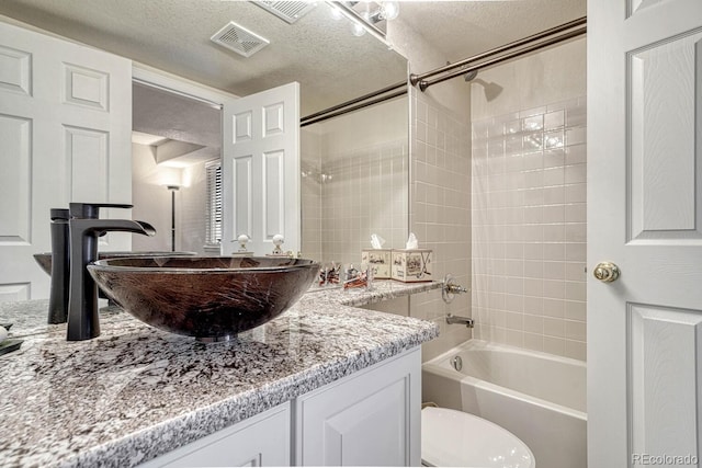 full bathroom featuring vanity, toilet, tiled shower / bath, and a textured ceiling