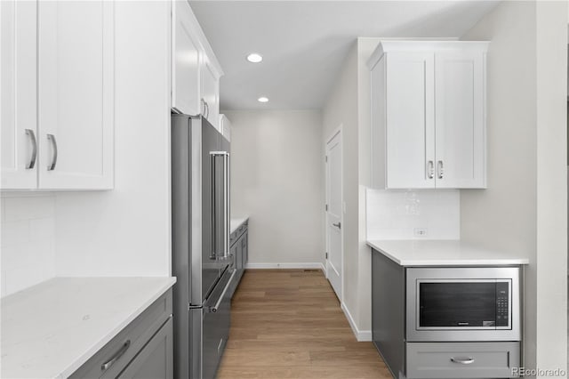 kitchen featuring appliances with stainless steel finishes, light hardwood / wood-style flooring, white cabinetry, and light stone countertops