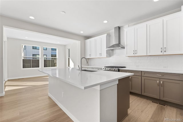 kitchen featuring wall chimney exhaust hood, a center island with sink, light wood-type flooring, white cabinets, and sink